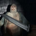 Image of a large, pale zombie facing the player in a dark, eerie corridor, with a close-up of a sharp combat knife being held in the foreground, ready for action.